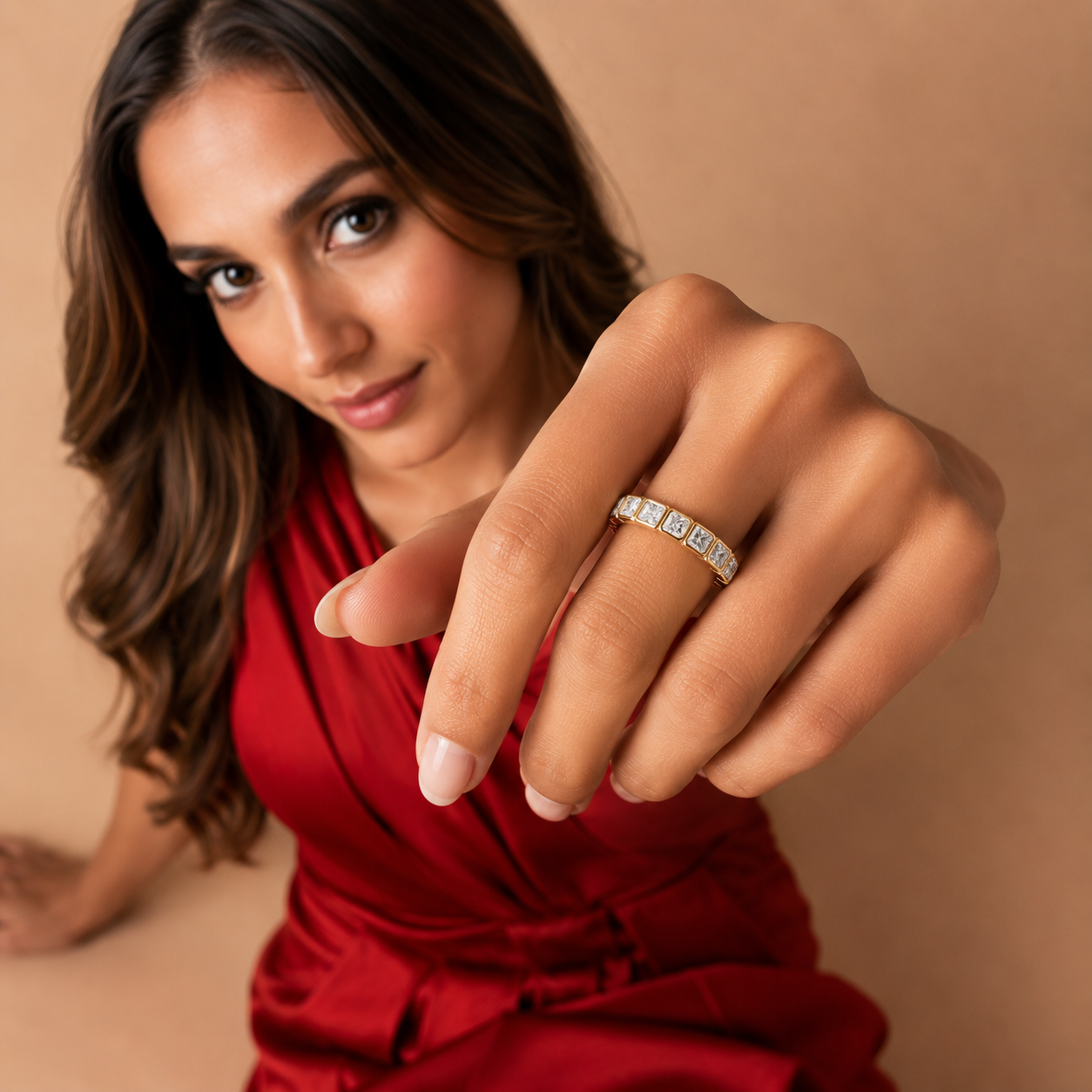 A woman wearing a silver band ring with small clear stones, shown in a close-up lifestyle shot against a warm beige background.