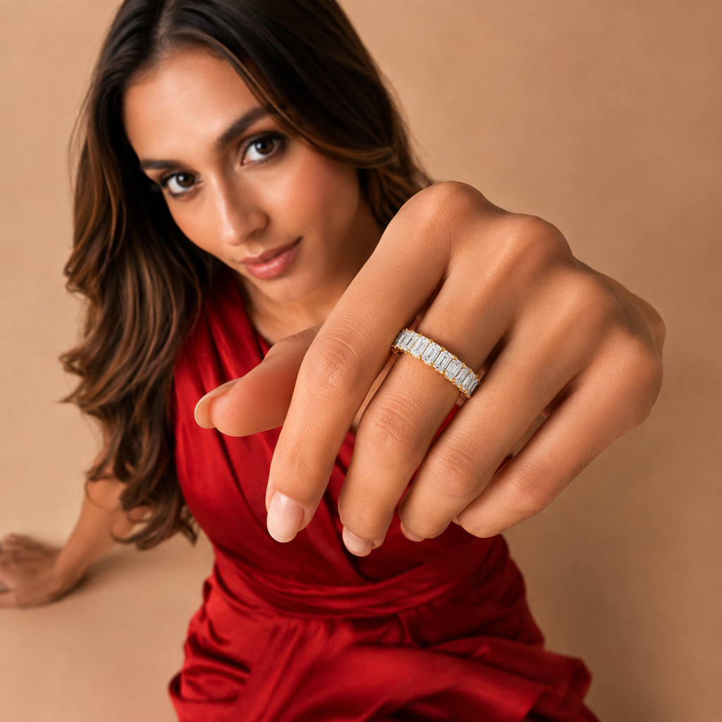 A woman in a red dress extends her hand toward the camera, wearing a silver band ring set with small clear stones against a warm beige background.