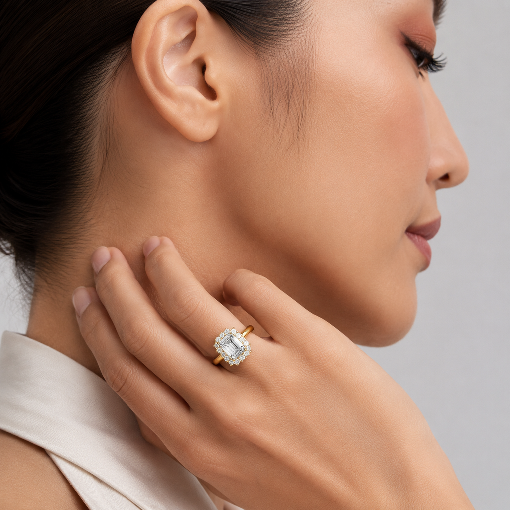 A close-up lifestyle shot of a woman wearing a gold ring with a large cushion-cut clear gemstone on her finger, with her hand resting near her neck.
