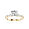 An emerald-cut diamond engagement ring in a Yellow-colored metal setting, featuring a pave band with small round diamonds, shot against a solid white background.