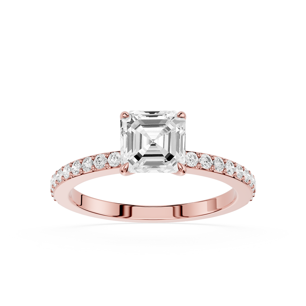 An emerald-cut diamond engagement ring in a Rose-colored metal setting, featuring a pave  band with small round diamonds, shot against a solid white background.