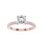 An emerald-cut diamond engagement ring in a Rose-colored metal setting, featuring a pave  band with small round diamonds, shot against a solid white background.