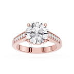 A rose gold engagement ring featuring a round-cut diamond center stone and small pavé diamonds along the split shank, set against a plain white background.