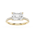 An emerald-cut diamond engagement ring in yellow gold with pavé-set diamonds on the band, shown on a clean white background.