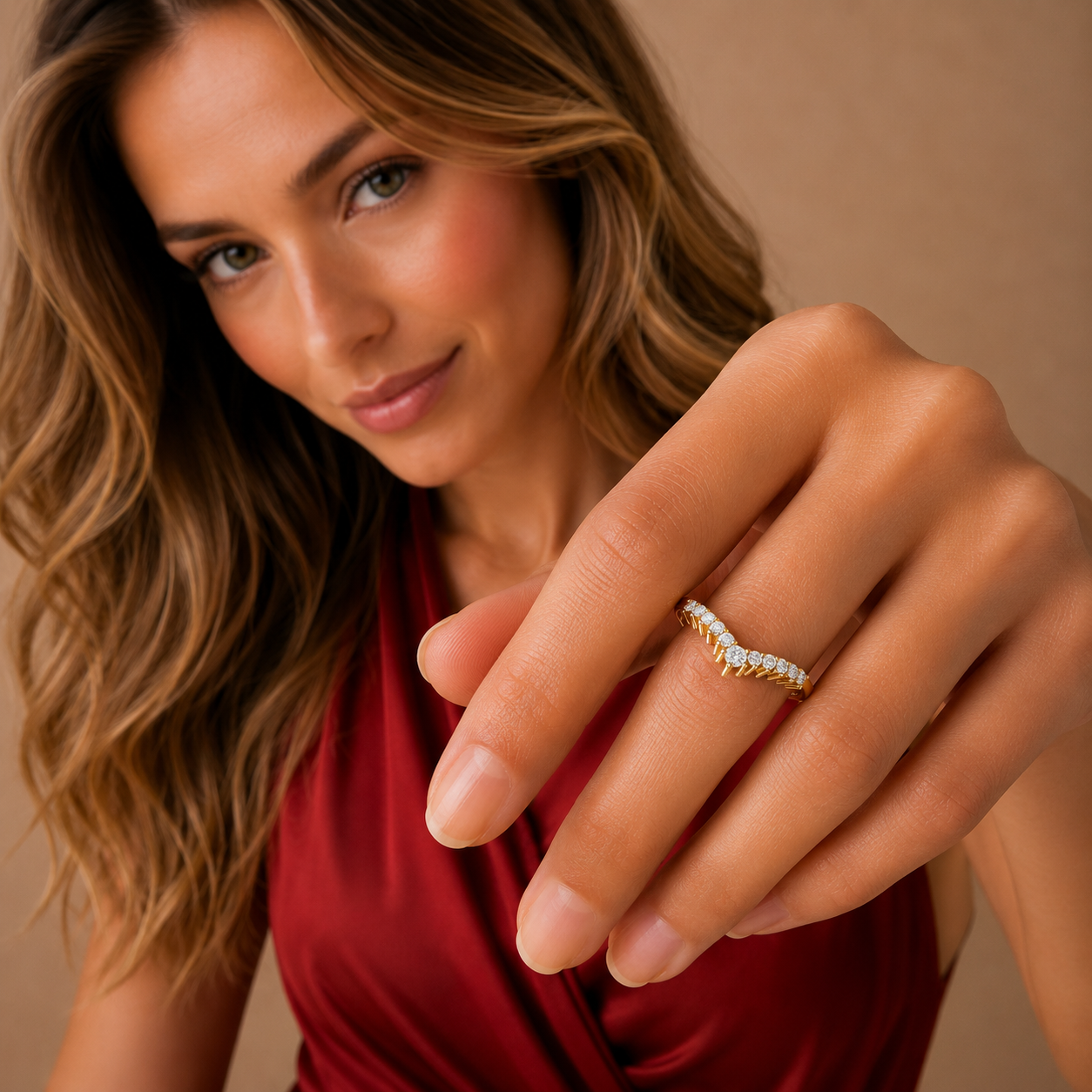 A close-up lifestyle shot of a woman wearing a wavy, channel-set diamond ring on her finger, wearing a red satin top against a warm beige background.
