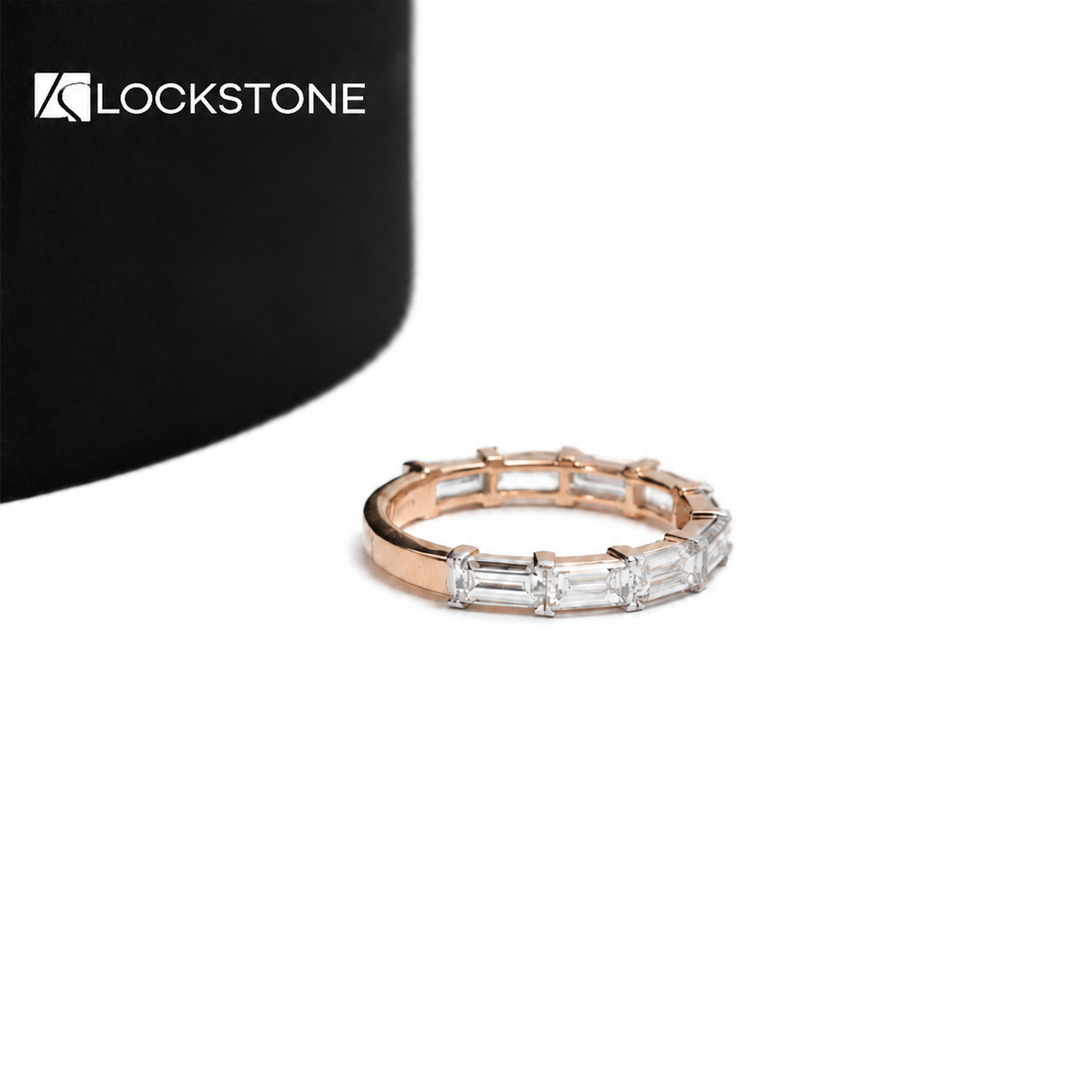 A row of step cut baguette diamonds lines the front of this rose gold anniversary ring with a slim polished band