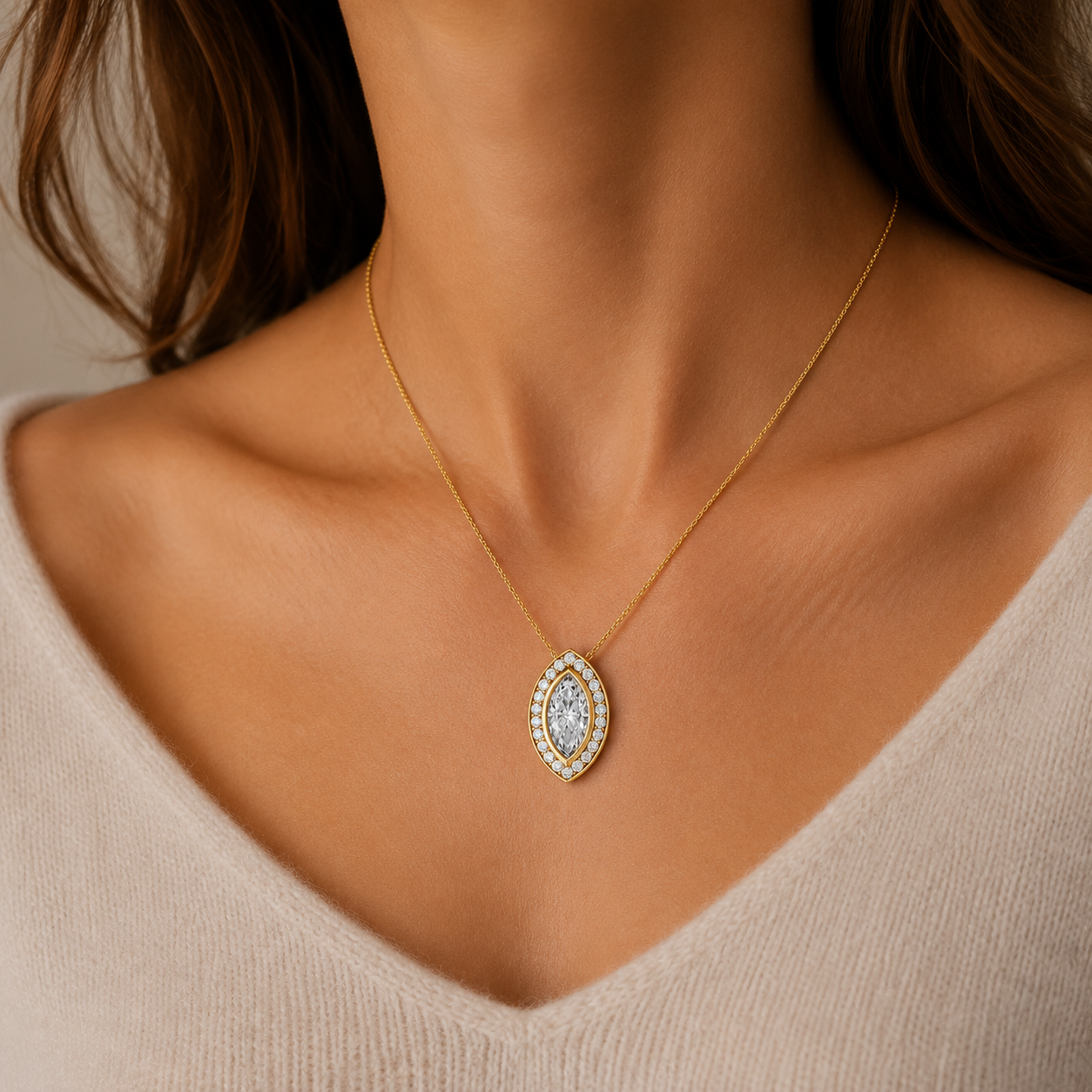 A close-up of a woman's neck and chest wearing a delicate gold chain necklace with a marquise-shaped pendant set with clear stones.