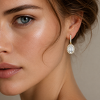 A close-up of a woman's face and ear wearing a gold drop earring with a large oval cluster of clear stones, set against a soft neutral background.