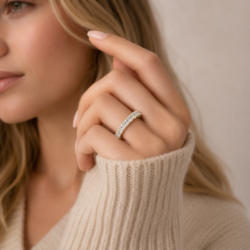A close-up lifestyle shot of a woman wearing a silver half-ring set with small clear stones, shown on her finger as she wears a beige ribbed knit sweater.