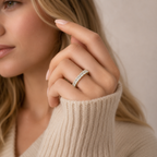 A close-up lifestyle shot of a woman wearing a silver half-ring set with small clear stones, shown on her finger as she wears a beige ribbed knit sweater.