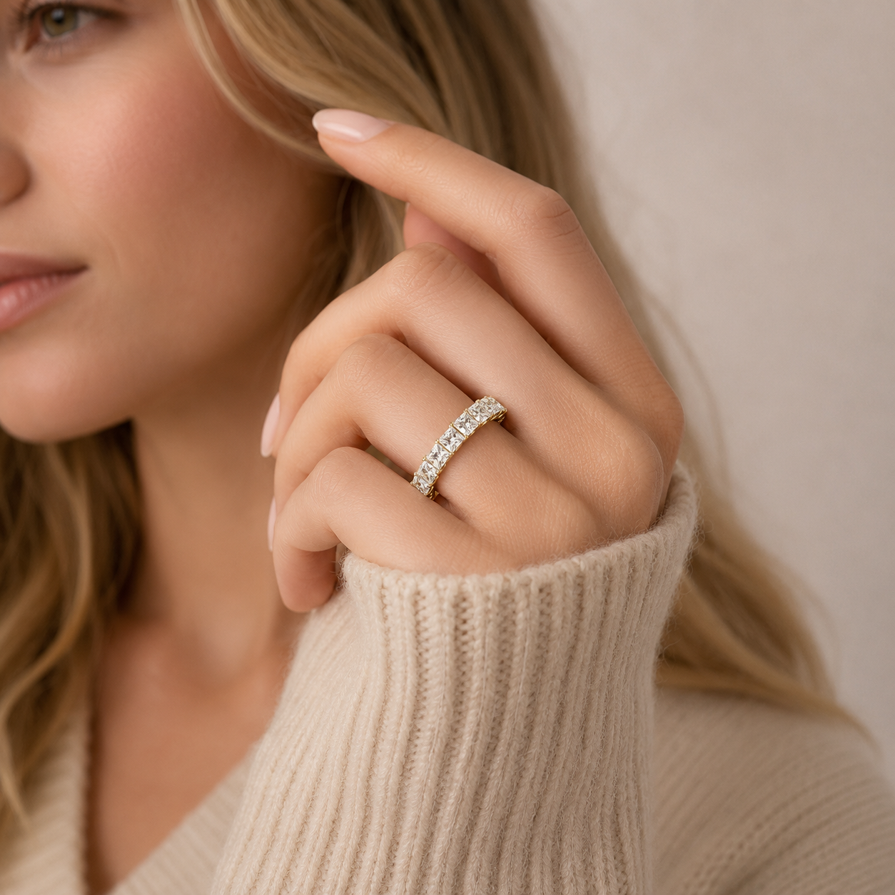 A close-up lifestyle shot of a woman wearing a silver half-ring set with small clear stones, shown on her finger as she wears a beige ribbed knit sweater.