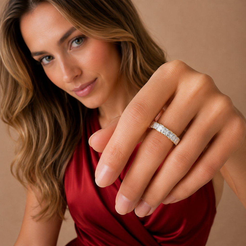 A woman wearing a silver band ring with small clear stones, shown in a close-up lifestyle shot against a warm beige background.