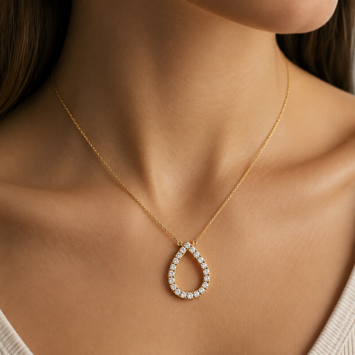 A close-up of a woman's neck and upper chest wearing a delicate gold chain necklace with a teardrop-shaped pendant set with small clear stones.