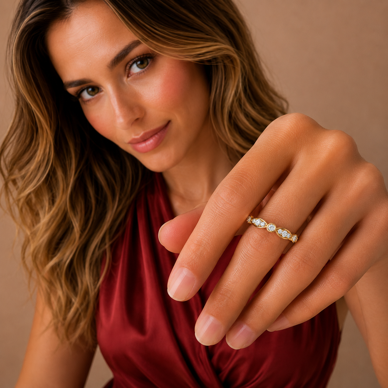 A close-up lifestyle shot of a woman wearing a delicate gold band ring with small clear stones, set against a warm beige background.