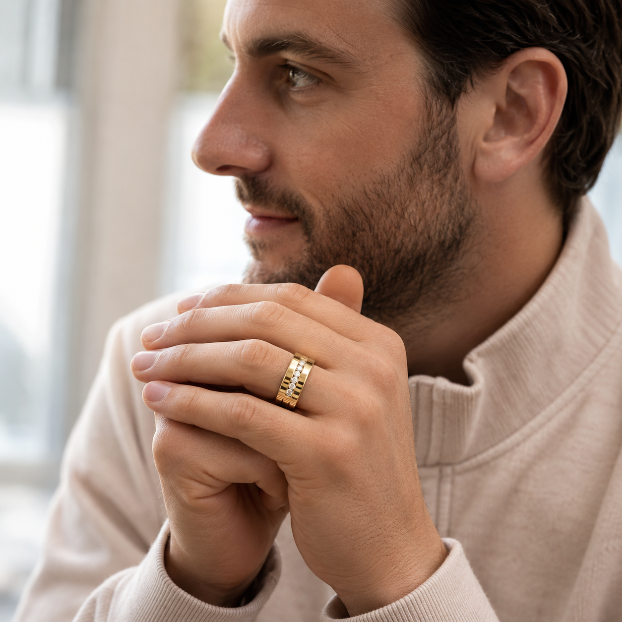 A man in a beige mock-neck sweater wearing a gold band ring with engraved lettering, shown in a close-up profile portrait.