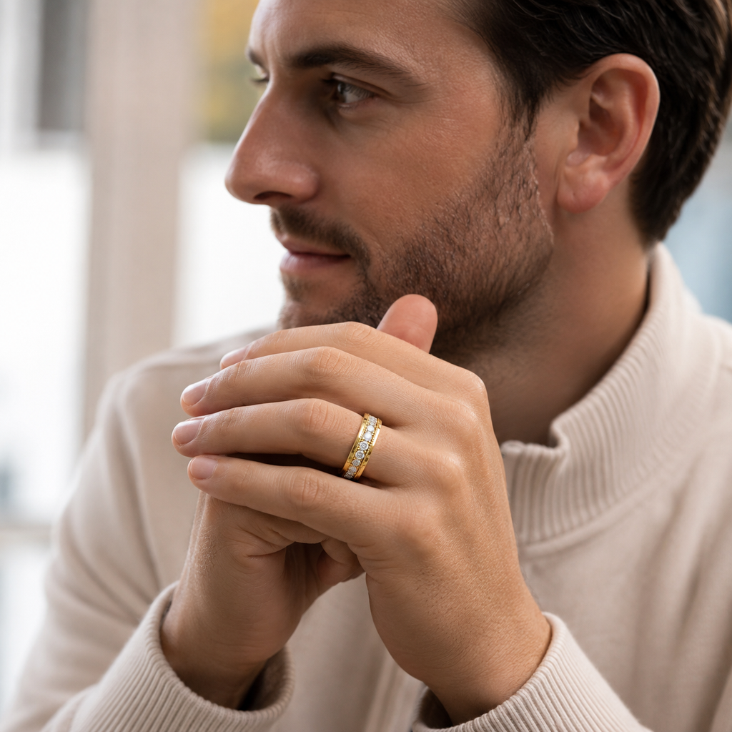 A close-up lifestyle shot of a man wearing a gold band ring with small clear stones on his ring finger, dressed in a cream-colored ribbed turtleneck sweater.