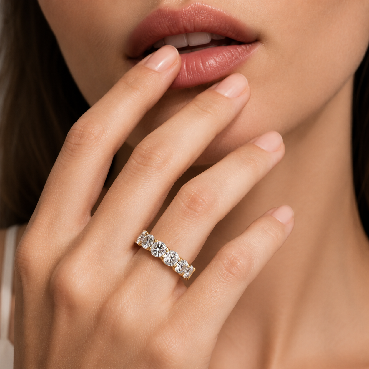 A close-up lifestyle shot of a woman's hand wearing a silver diamond eternity ring, with her hand resting near her lips.
