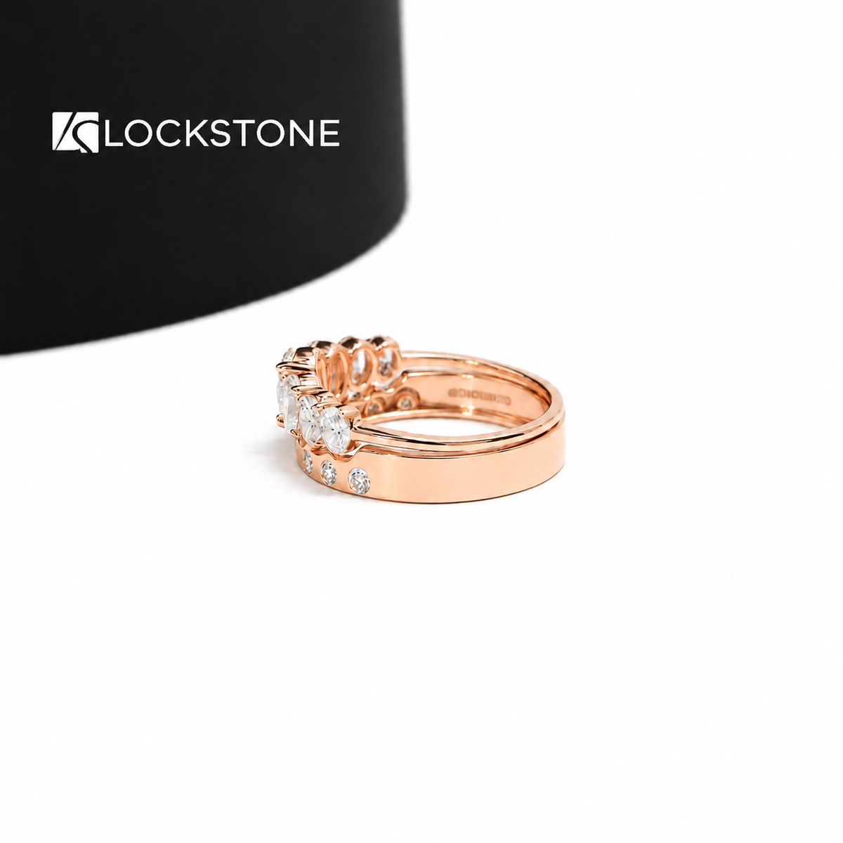 Five oval cut diamonds form a graduated row above a rose gold stacking band decorated with small round diamond accents