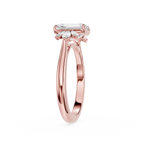 A rose gold engagement ring featuring an emerald-cut center stone and smaller marquise-cut side stones, shown on a clean white background.