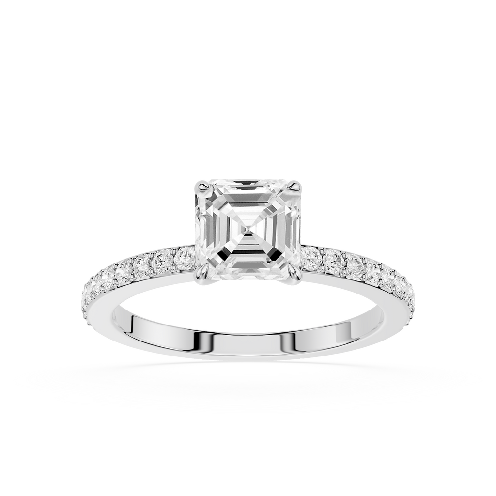 An emerald-cut diamond engagement ring in a silver-colored metal setting, featuring a pavé band with small round diamonds, shot against a solid white background.