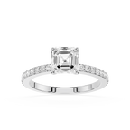 An emerald-cut diamond engagement ring in a silver-colored metal setting, featuring a pavé band with small round diamonds, shot against a solid white background.